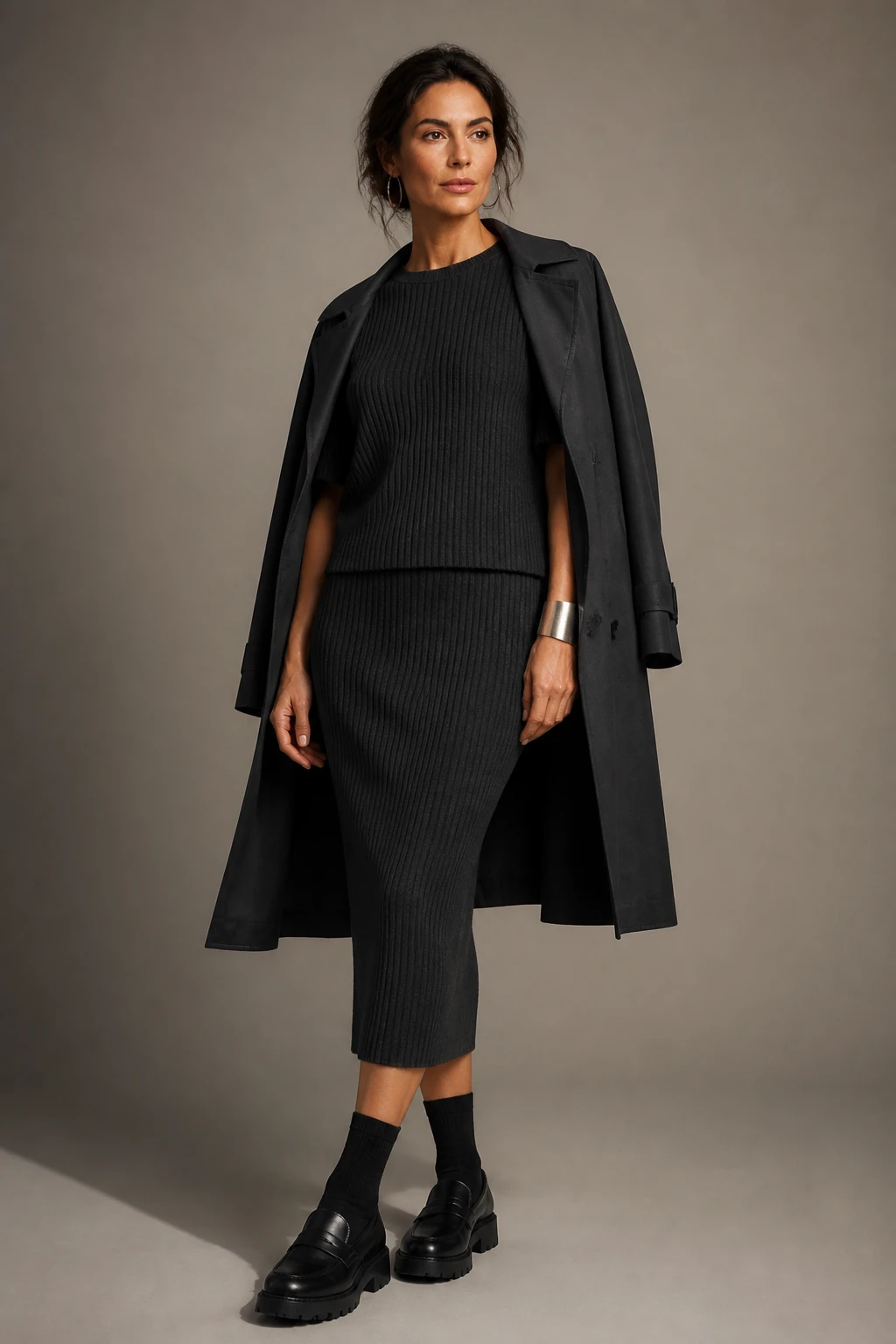An elegant mid-30s woman wears a charcoal monochrome ribbed knit set with chunky loafers and subtle jewelry for a streamlined look.