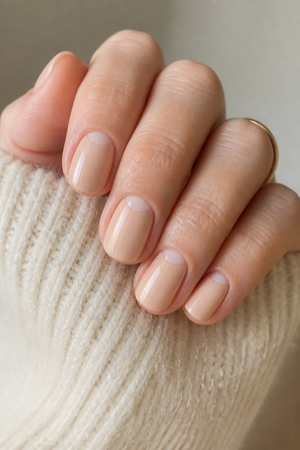 Short rounded nails in soft beige nude with peach undertones and a negative-space moon on a chic woman in her mid-40s.