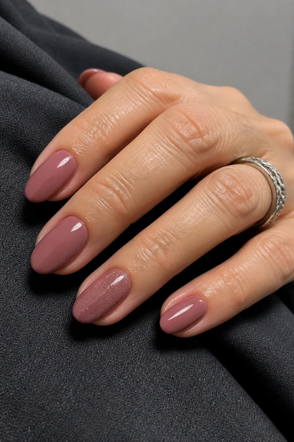 Soft almond nails in glossy rosy mauve with a subtle ring-finger micro-sparkle on a stylish woman in her mid-40s.