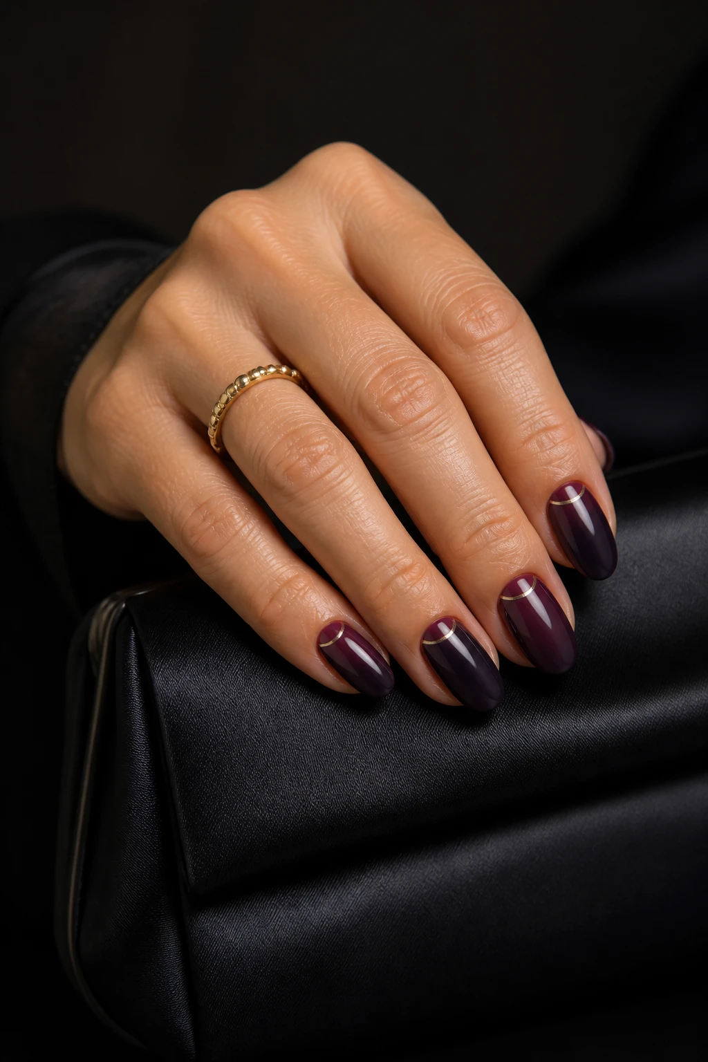 Short-medium almond nails in deep blackberry gloss with a subtle metallic cuticle stripe on a chic woman in her mid-40s.