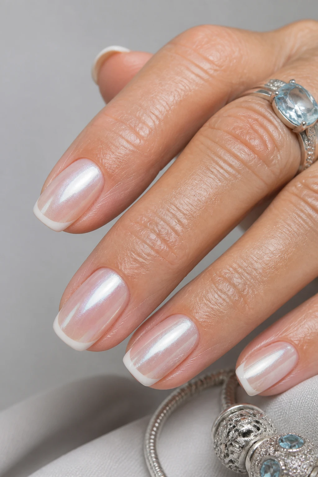 Oyster glaze French with pearl chrome and delicate ivory tips on a chic woman in her 50s.