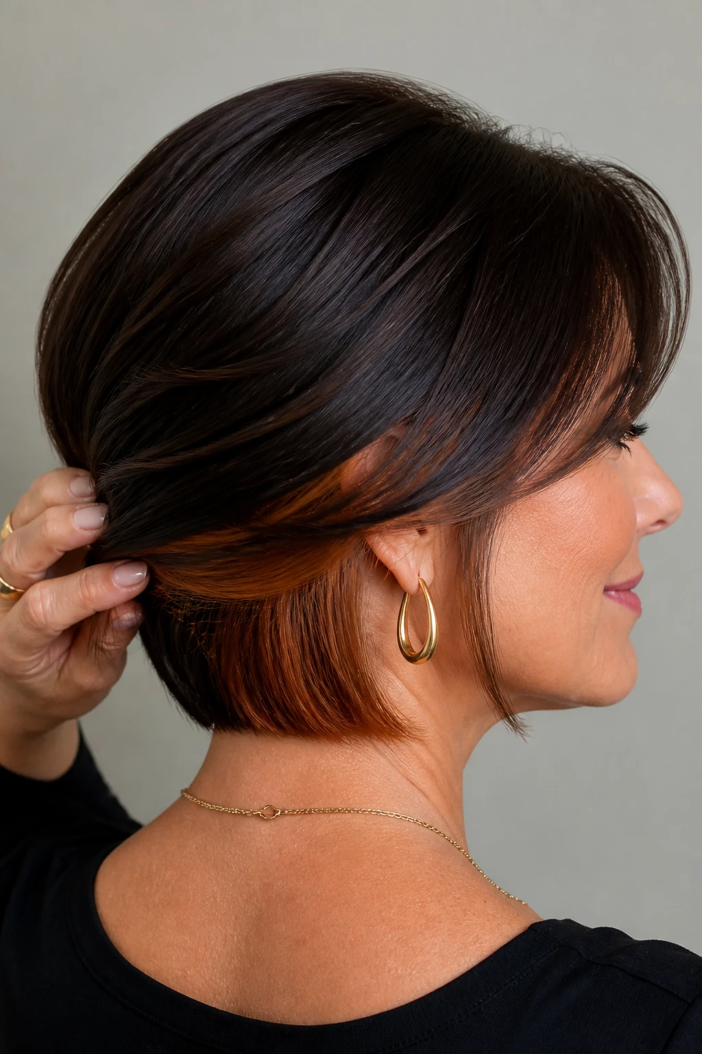 Espresso hair with amber peekaboo underlights subtly flashes warmth on a sophisticated woman in her mid-50s.