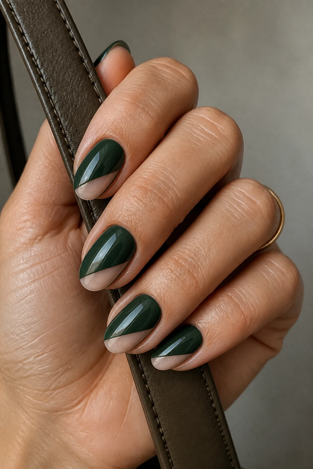 Short-medium almond nails in forest green with a satin finish and negative-space diagonal on a refined woman in her mid-40s.
