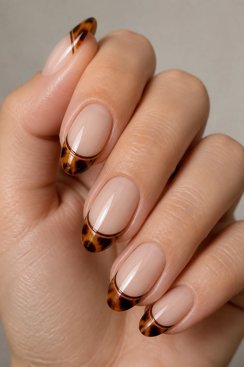 Short almond nails with sheer base and glossy tortoiseshell tips defined by a thin cocoa line.