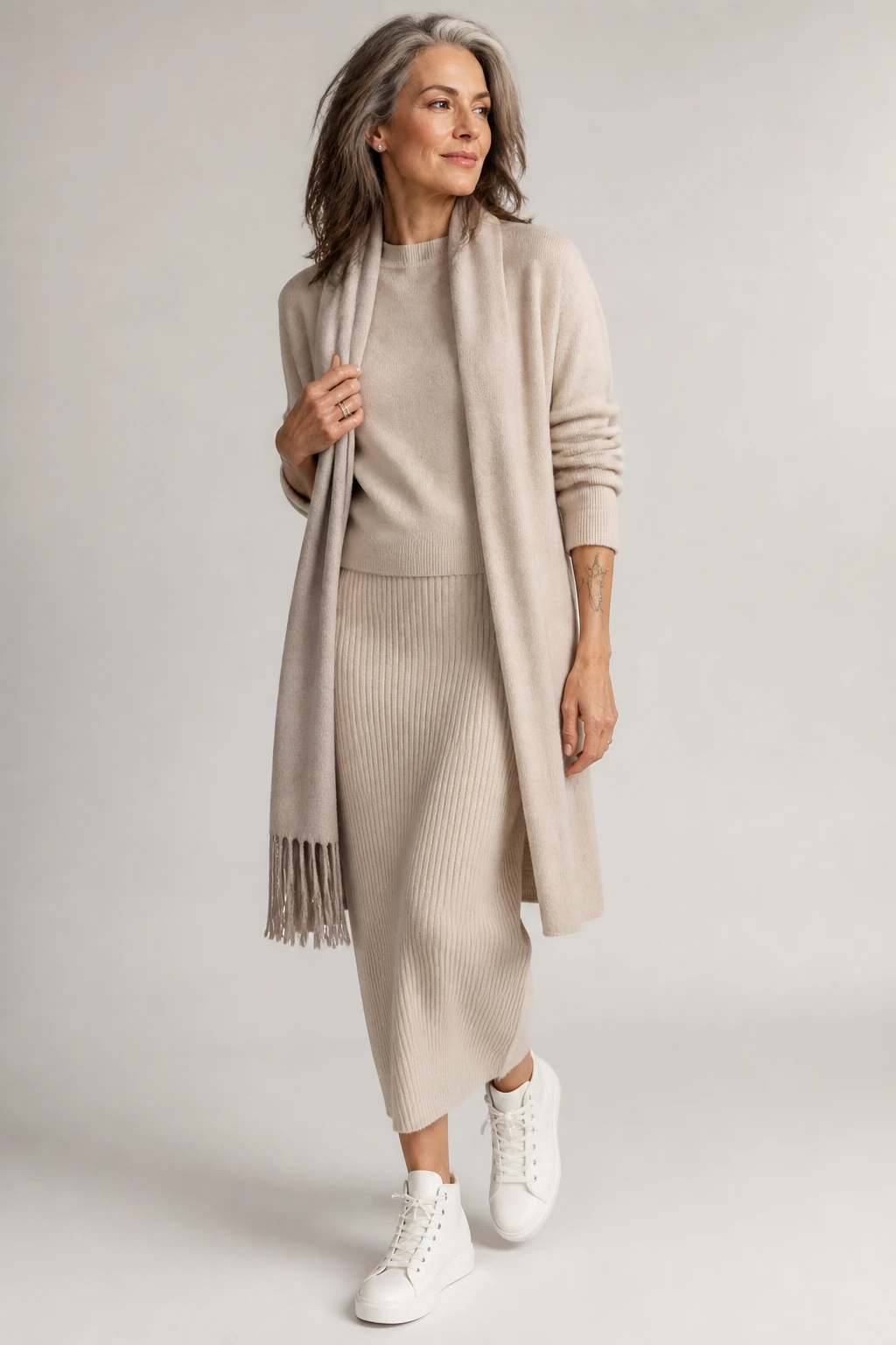A chic woman in her late 50s wears a stone knit set with a coatigan and sleek leather high-top sneakers.