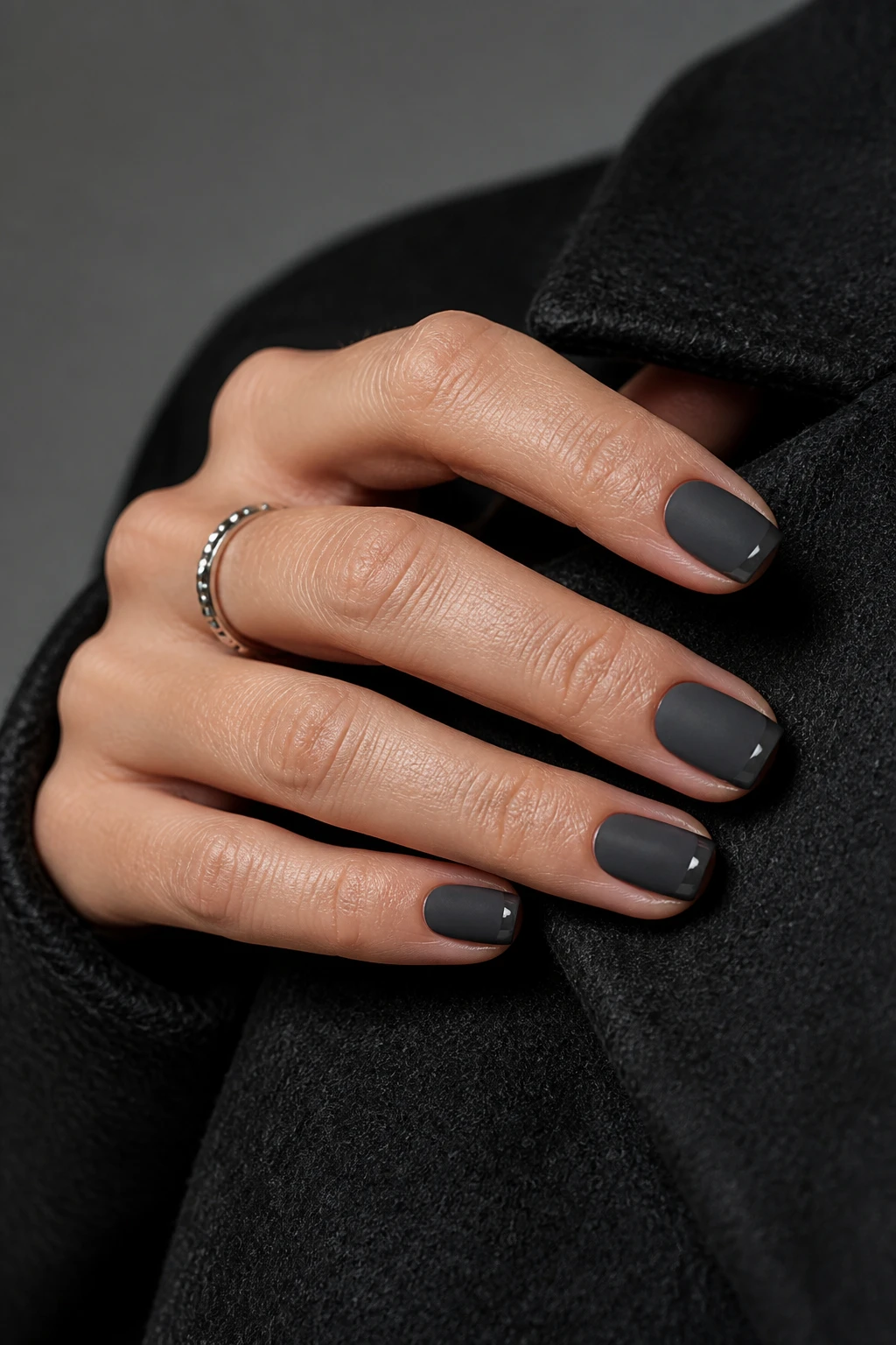Charcoal gray squoval nails with a soft matte finish and glossy reverse French tips on a chic woman in her mid-40s.